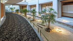 A modern hotel interior with a curved carpeted walkway, potted plants, and a traditional Japanese aesthetic. - APA Hotel & Resort Kaga Katayamazu Onsen Kasuikyo (Kaga)