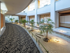 A modern hotel interior with a curved carpeted walkway, potted plants, and a traditional Japanese aesthetic. - APA Hotel & Resort Kaga Katayamazu Onsen Kasuikyo (Kaga)