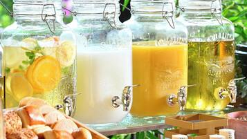 Four glass jars with metal clasps, each containing a different beverage and garnished with citrus slices. A tray with bread rolls is in the foreground.