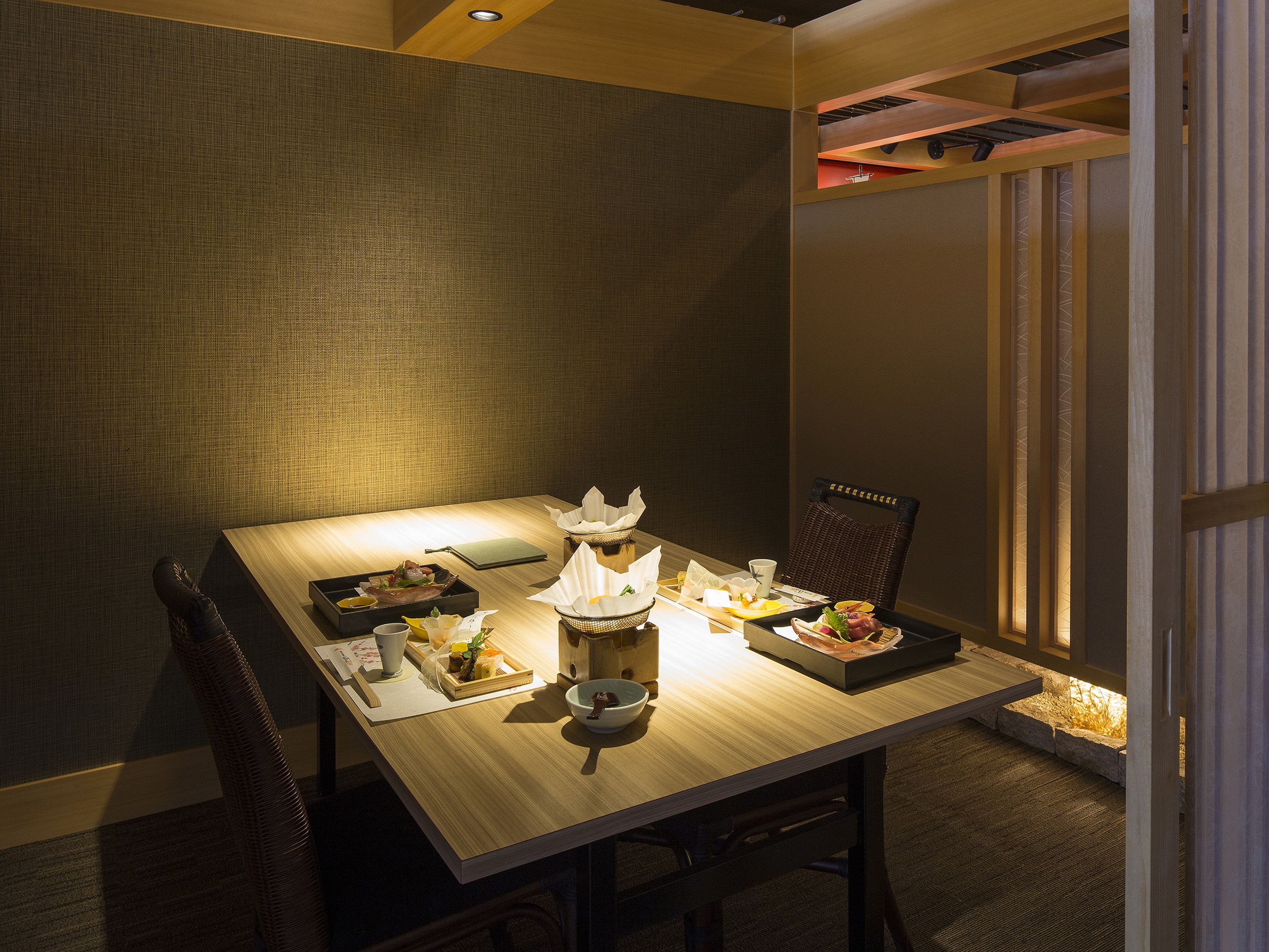 Una mesa de comedor con diversos platos y una vela, en una habitación con pared texturizada y una ventana con persianas verticales.