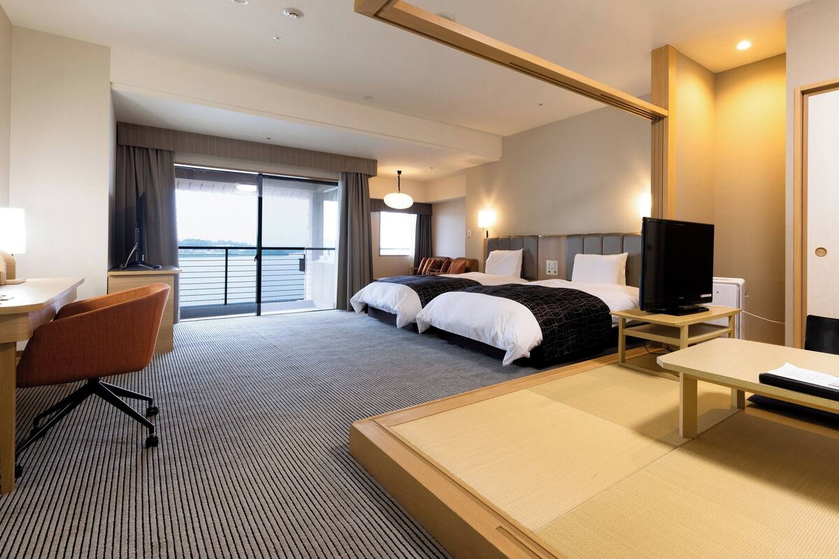 A hotel room with a bed, a desk, a chair, a television, and a view of the outside.