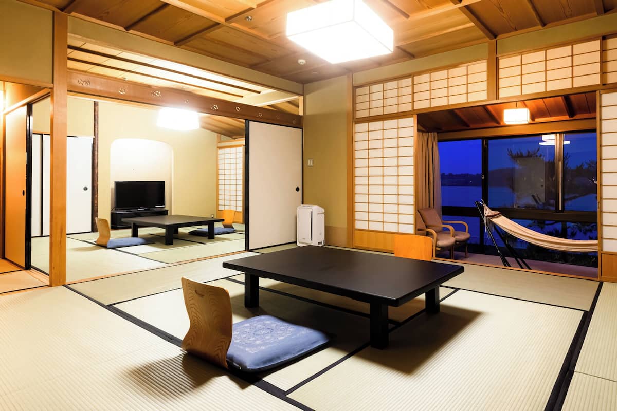 A traditional Japanese room with tatami flooring, a low table, a television, and a view of the outdoors.