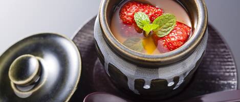 A bowl of soup with strawberries and mint leaves, accompanied by a spoon and a lid.