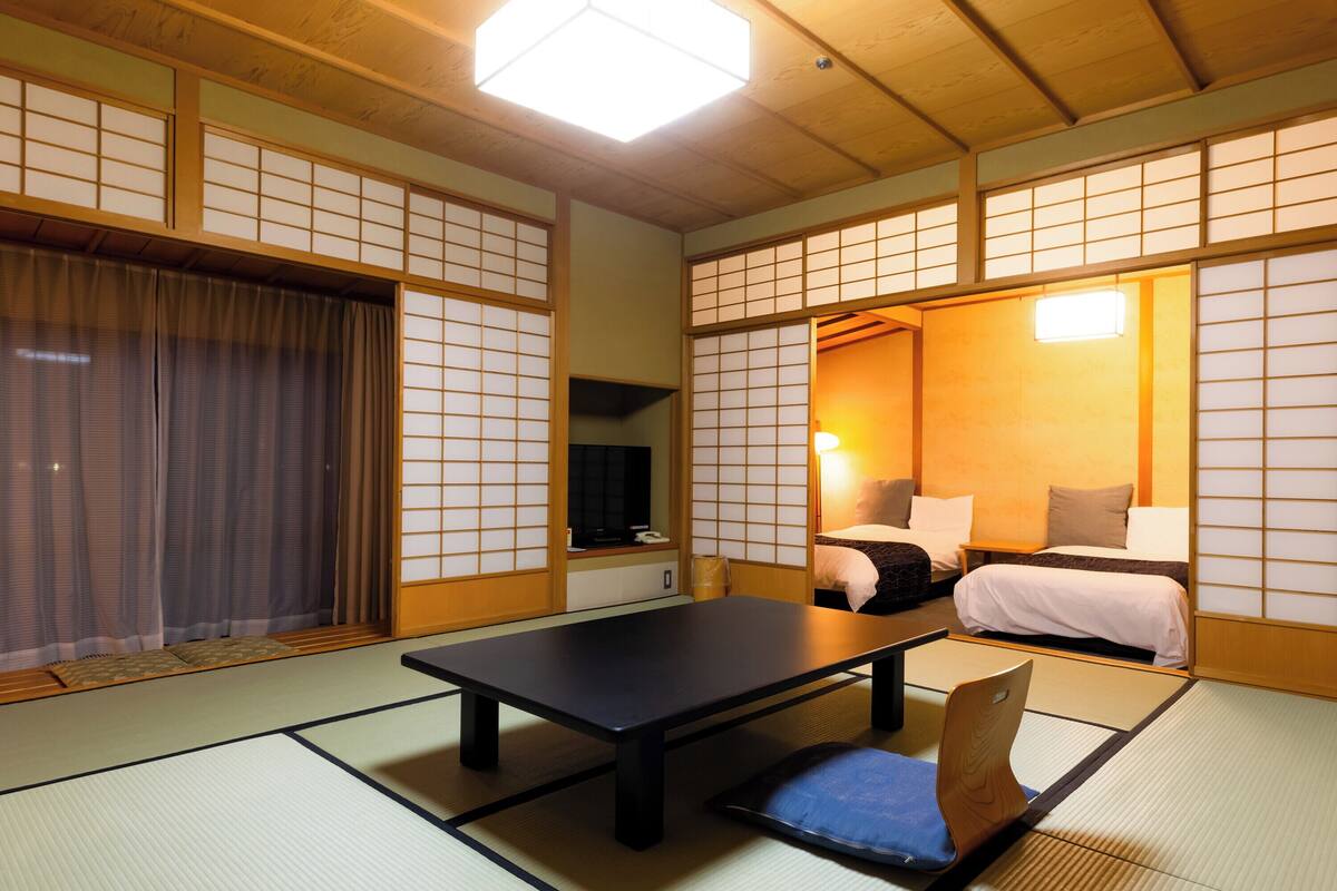 A traditional Japanese room with tatami flooring, a low table, and a bed with pillows.