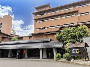A building with a traditional Japanese architectural style, featuring a tiled roof and a large tree in front.