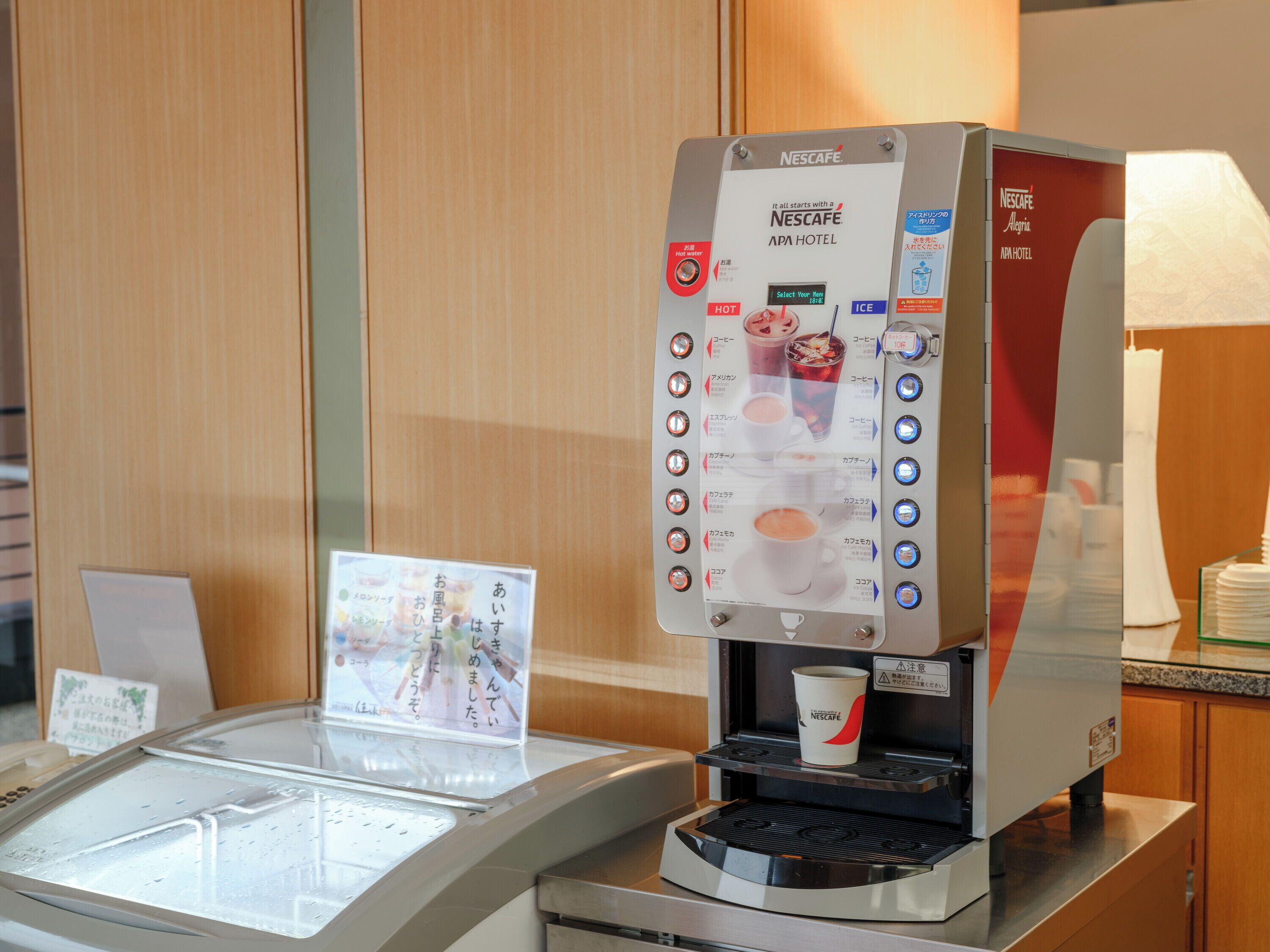 Máquina de café Nescafe com visor de menu, porta-copos e uma pequena placa com texto em japonês.