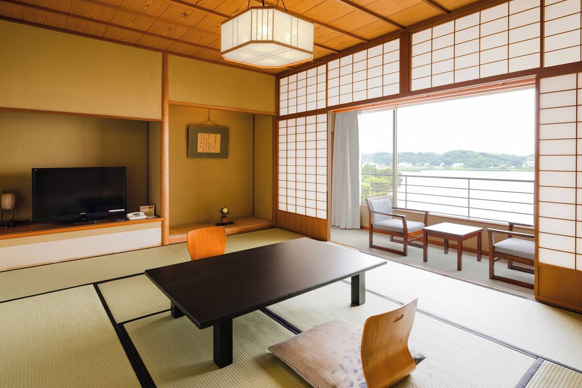 A traditional Japanese room with tatami flooring, a low table, a sofa, and a television on a shelf.