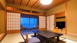 A traditional Japanese room with tatami flooring, a low table, chairs, and a sliding door leading to a balcony with a view. - APA Hotel & Resort Kaga Katayamazu Onsen Kasuikyo (Kaga)