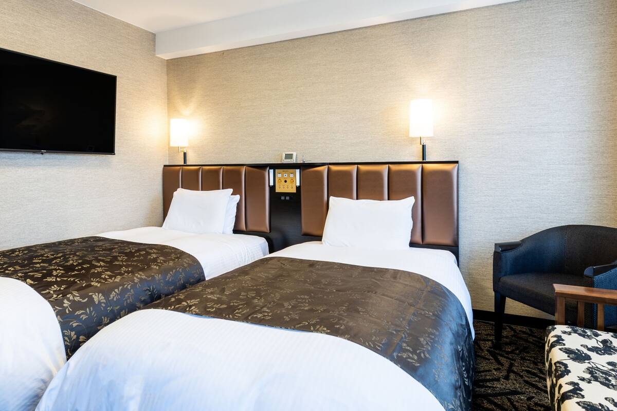 Une chambre d’hôtel avec deux lits, un téléviseur à écran plat fixé au mur et un bureau avec une chaise.