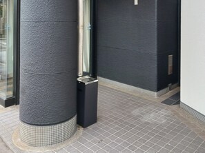 Un coin d’un bâtiment avec un mur noir à texture, un poteau métallique et un sol carrelé.