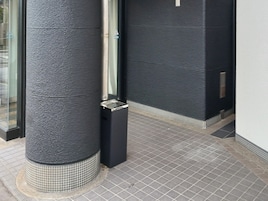 Esquina de un edificio con un muro negro texturizado, un poste metálico y un piso de baldosas.