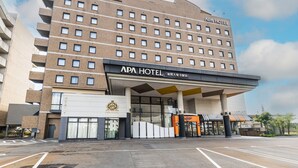 A multi-story hotel with a prominent 'APA HOTEL' sign, a covered entrance, and a parking lot.