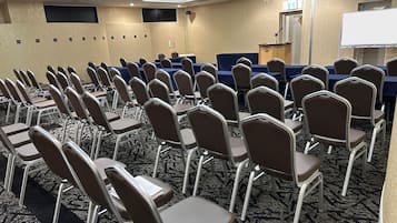 A conference room with rows of chairs, tables, a podium, and a whiteboard.