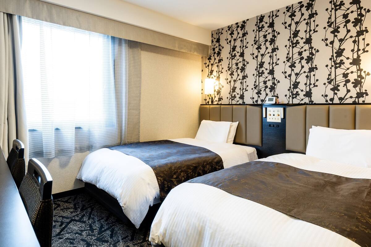 Une chambre d’hôtel avec deux lits, un bureau et une grande fenêtre avec des rideaux.