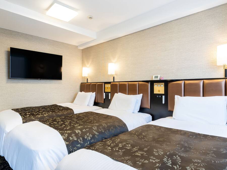 Une chambre d’hôtel avec deux lits, un téléviseur à écran plat fixé au mur et deux lampes murales.