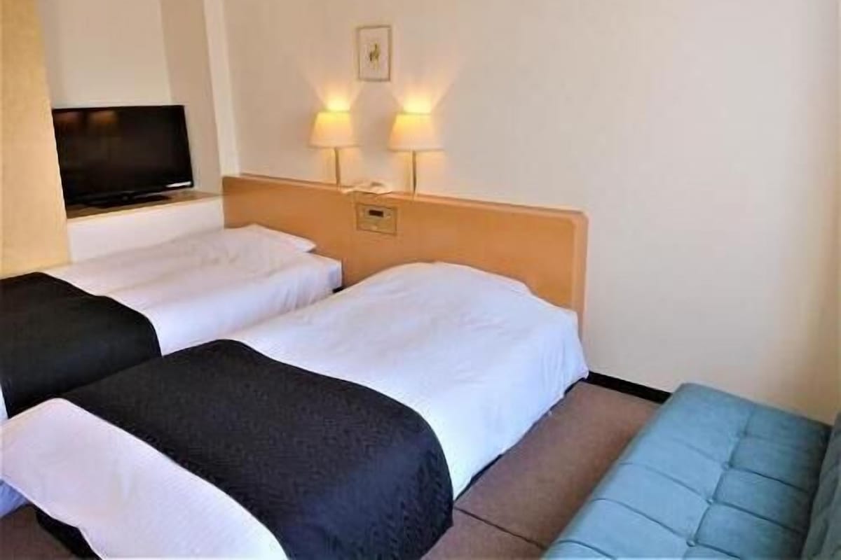 Une chambre d’hôtel avec deux lits, une télévision, deux lampes fixées au mur et un canapé bleu.