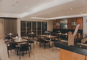 Interior modern d'un restaurant amb diverses taules i caires per a dinar, una barra i una finestra gran.