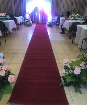 Un tapis rouge bordant un couloir menant à une scène surmontée d’un décor, de part et d’autre duquel se trouvent des tables ornées de compositions florales.