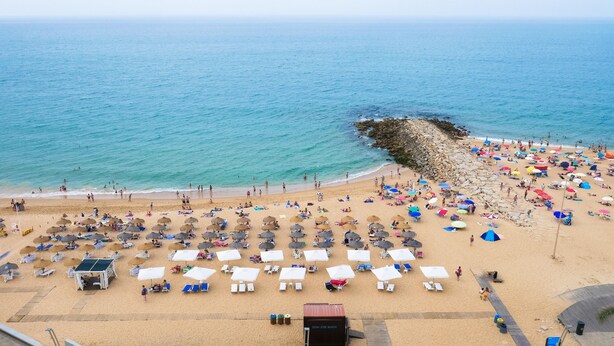A beach with numerous umbrellas and sun loungers, a rocky breakwater, and a clear view of the sea. - Algardia Apartments (Loulé)