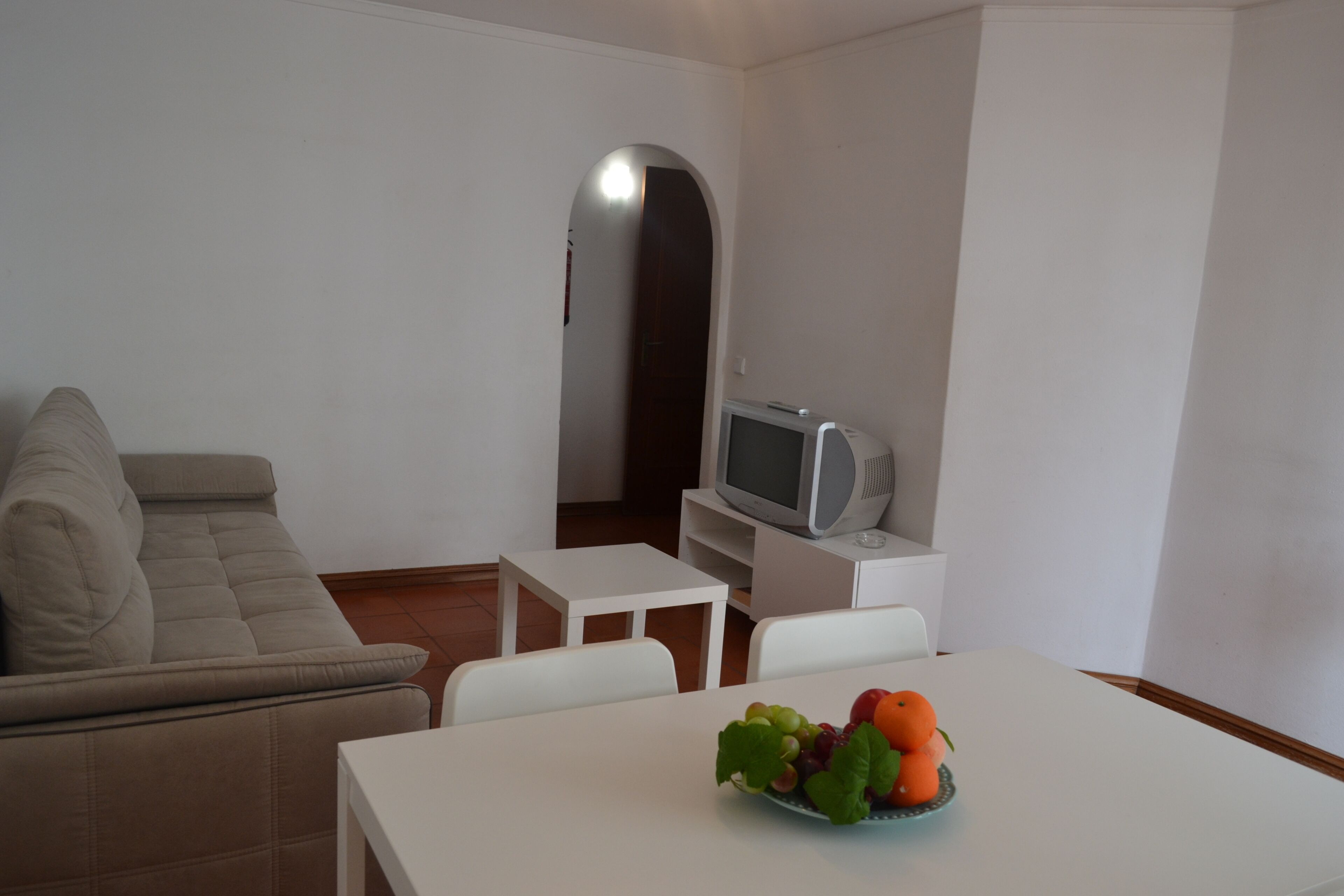 A living room with a sofa, a small table, a television, and a fruit bowl.