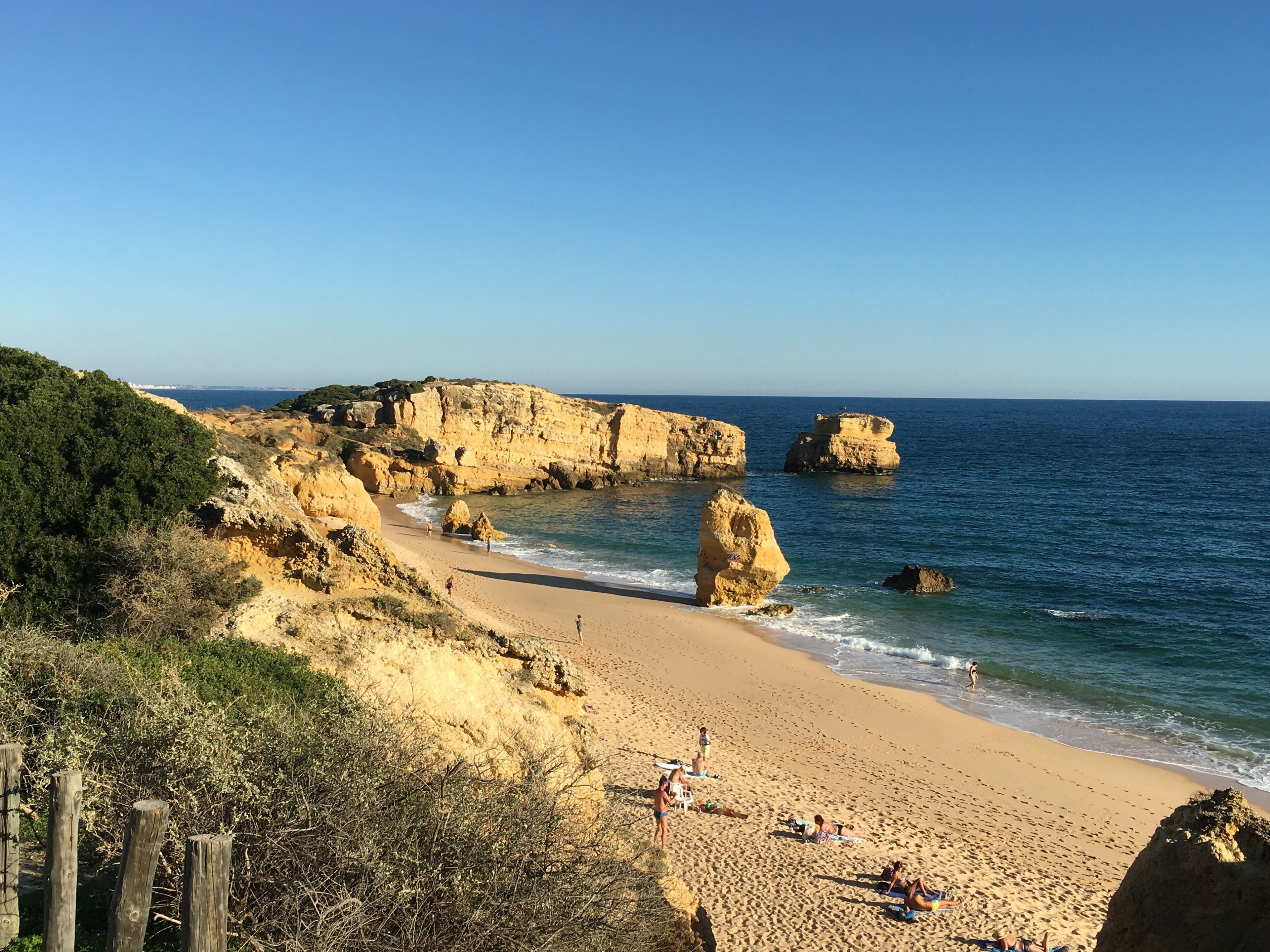A beach with rocky cliffs, clear blue sky, and calm sea.
