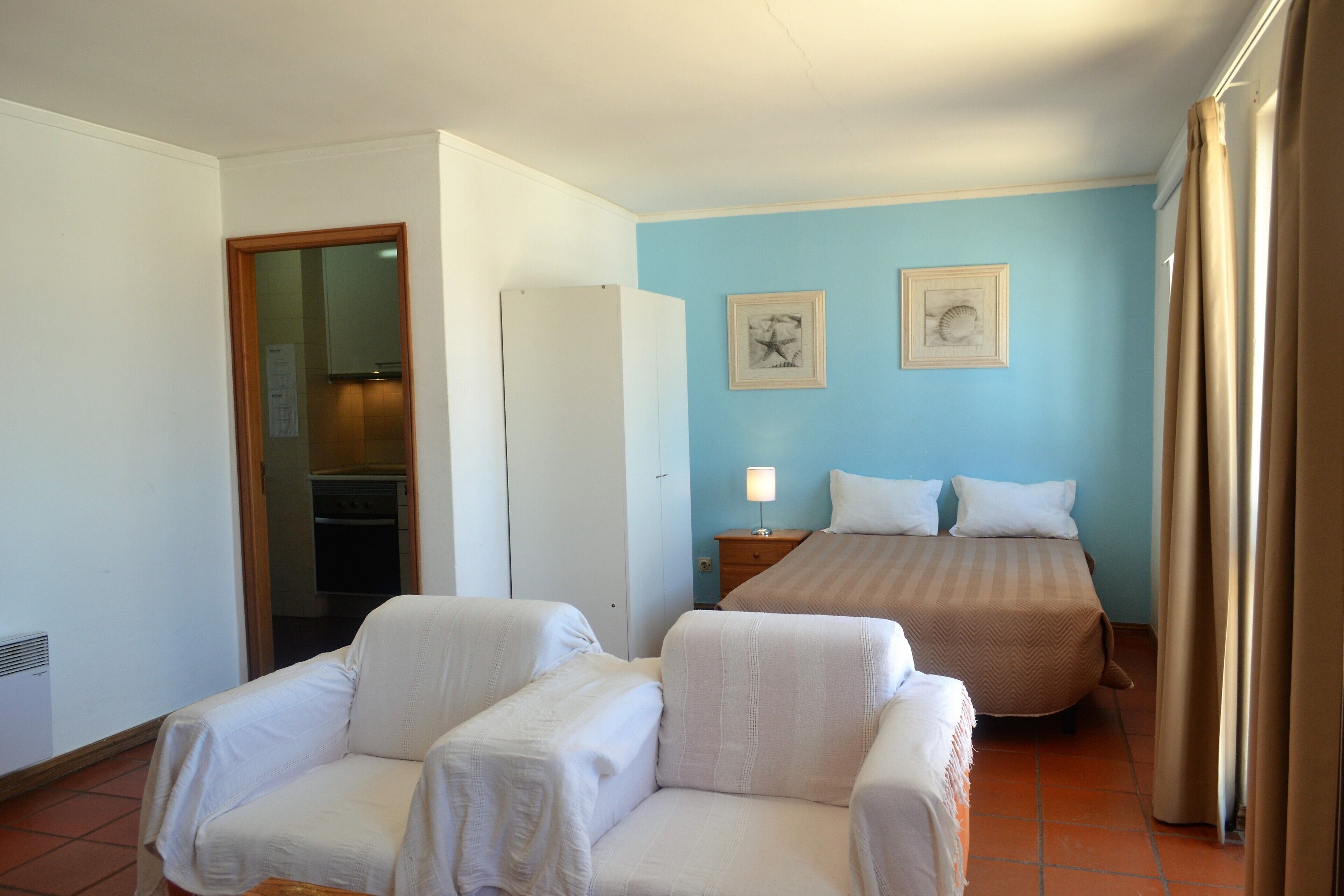 A hotel room with two single beds, a sitting area with two chairs, a nightstand with a lamp, and two framed pictures on the wall.