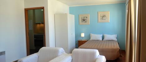 A hotel room with two single beds, a sitting area with two chairs, a nightstand with a lamp, and two framed pictures on the wall.