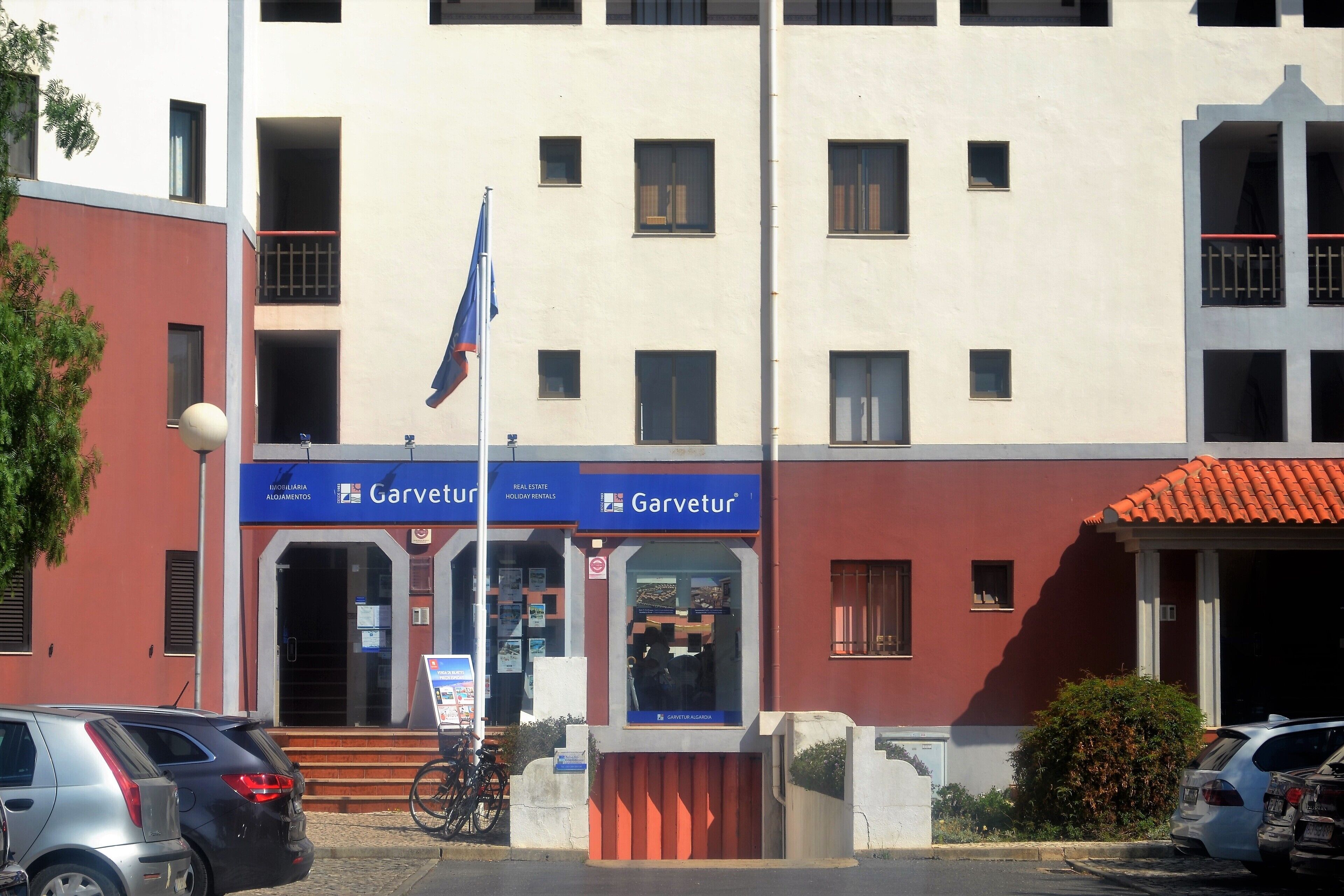 A Garvetur real estate and holiday rentals building with a red facade, multiple windows, and a flag.