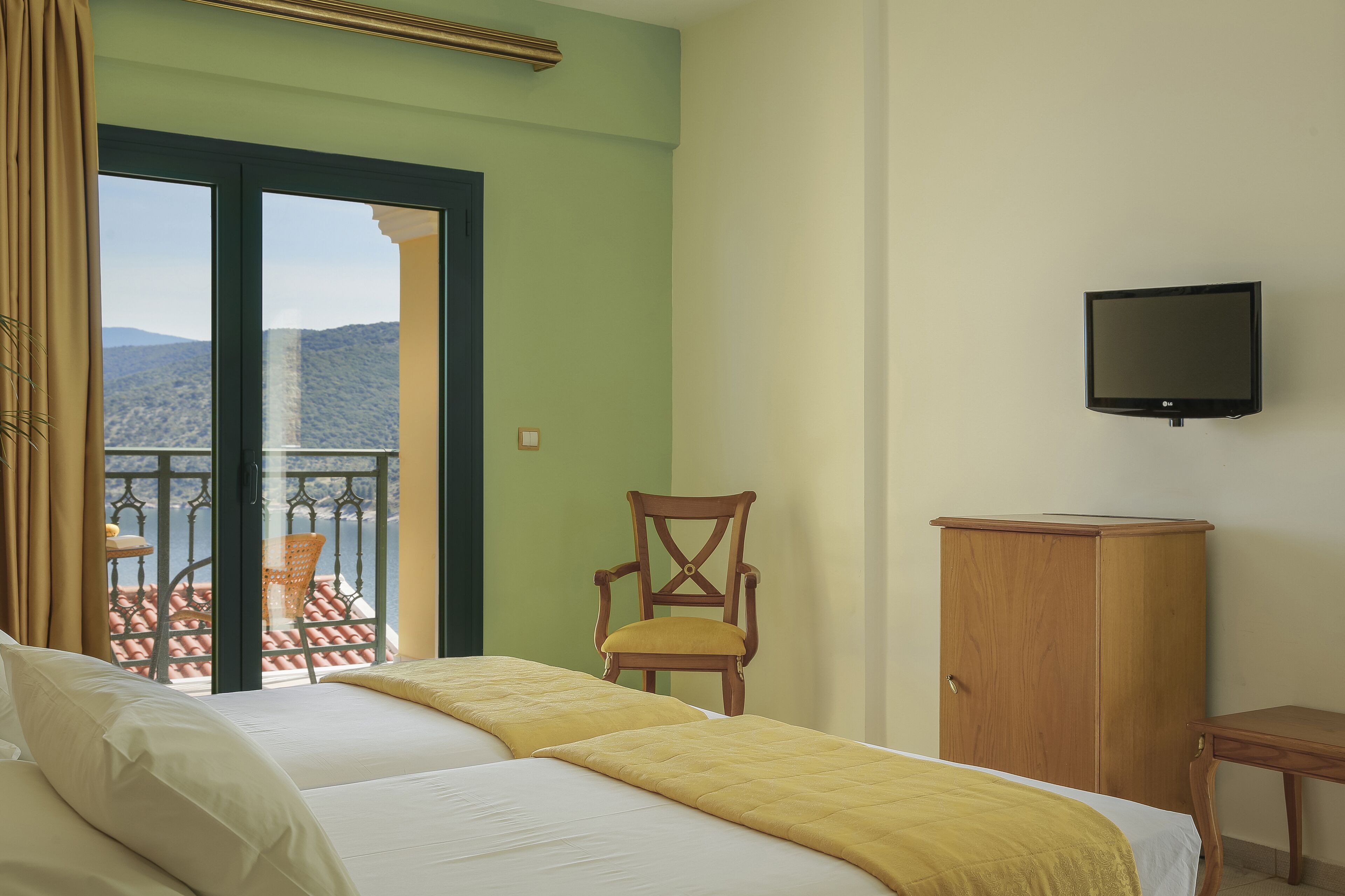 Een hotelkamer met twee bedden, een houten stoel, een televisie en uitzicht op de bergen door een balkondeur.