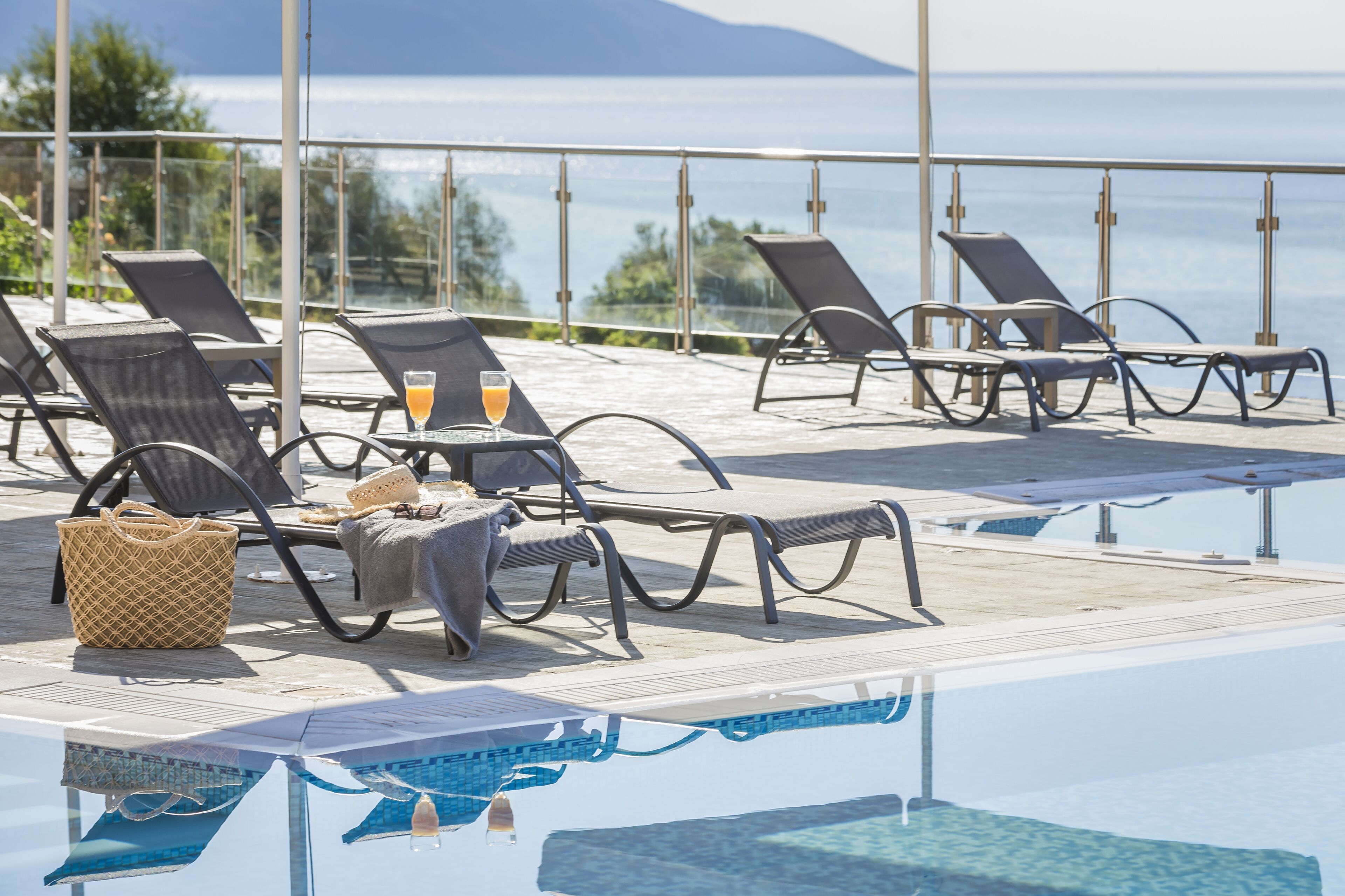 Area piscina con lettini, un tavolino con una bevanda e vista sul mare.