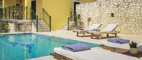A pool area with lounge chairs and a stone wall.