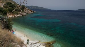 Una playa costera con agua turquesa cristalina, terreno rocoso y algunas personas disfrutando del lugar.