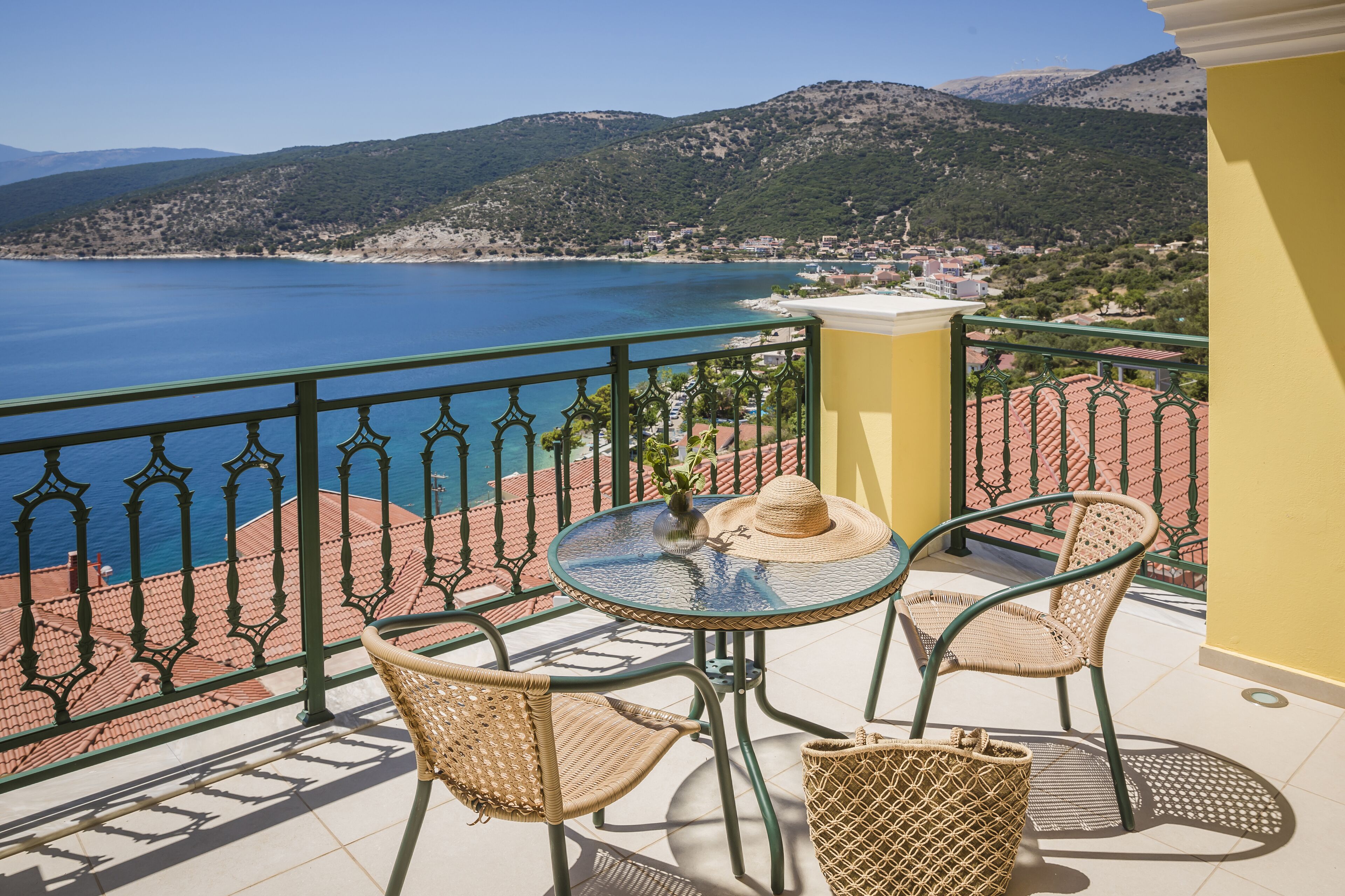 A balcony with wicker chairs, a table, and a view of a coastal landscape.