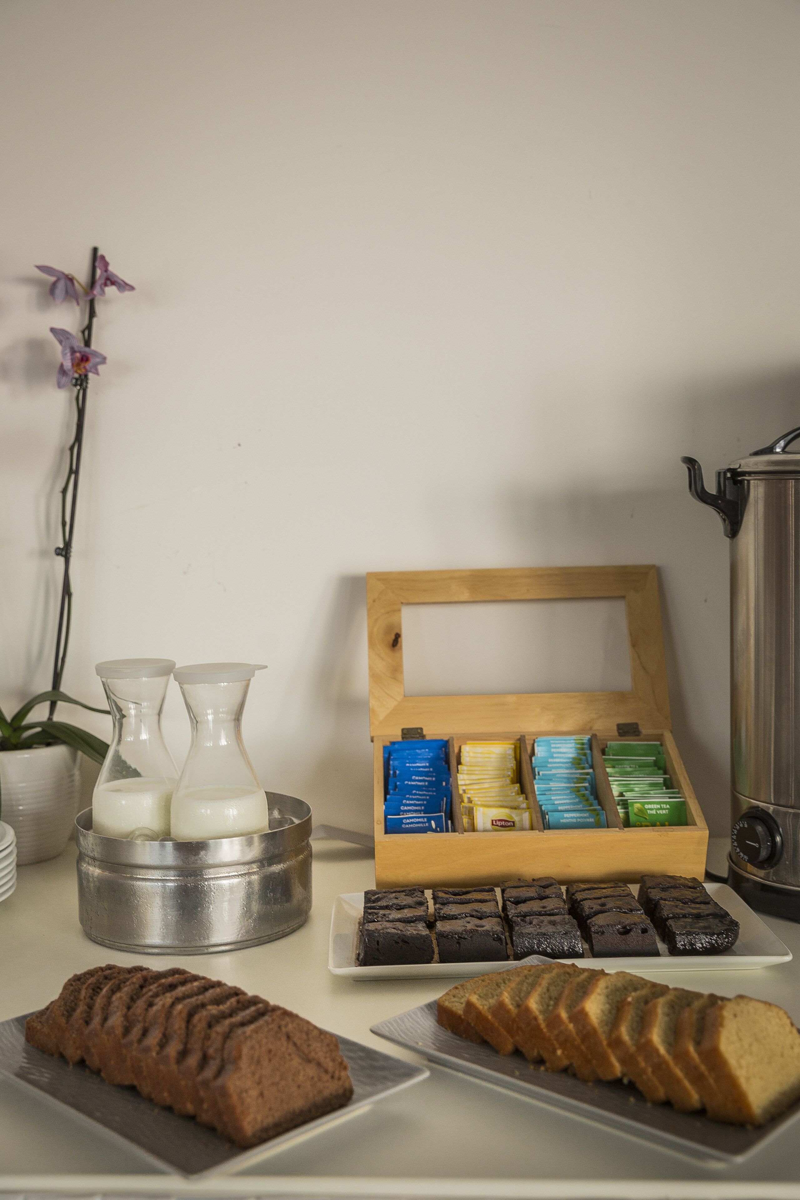 Una encimera de cocina con hogaza de pan, un plato de brownies, una caja de madera con bolsitas de té y dos recipientes de vidrio.