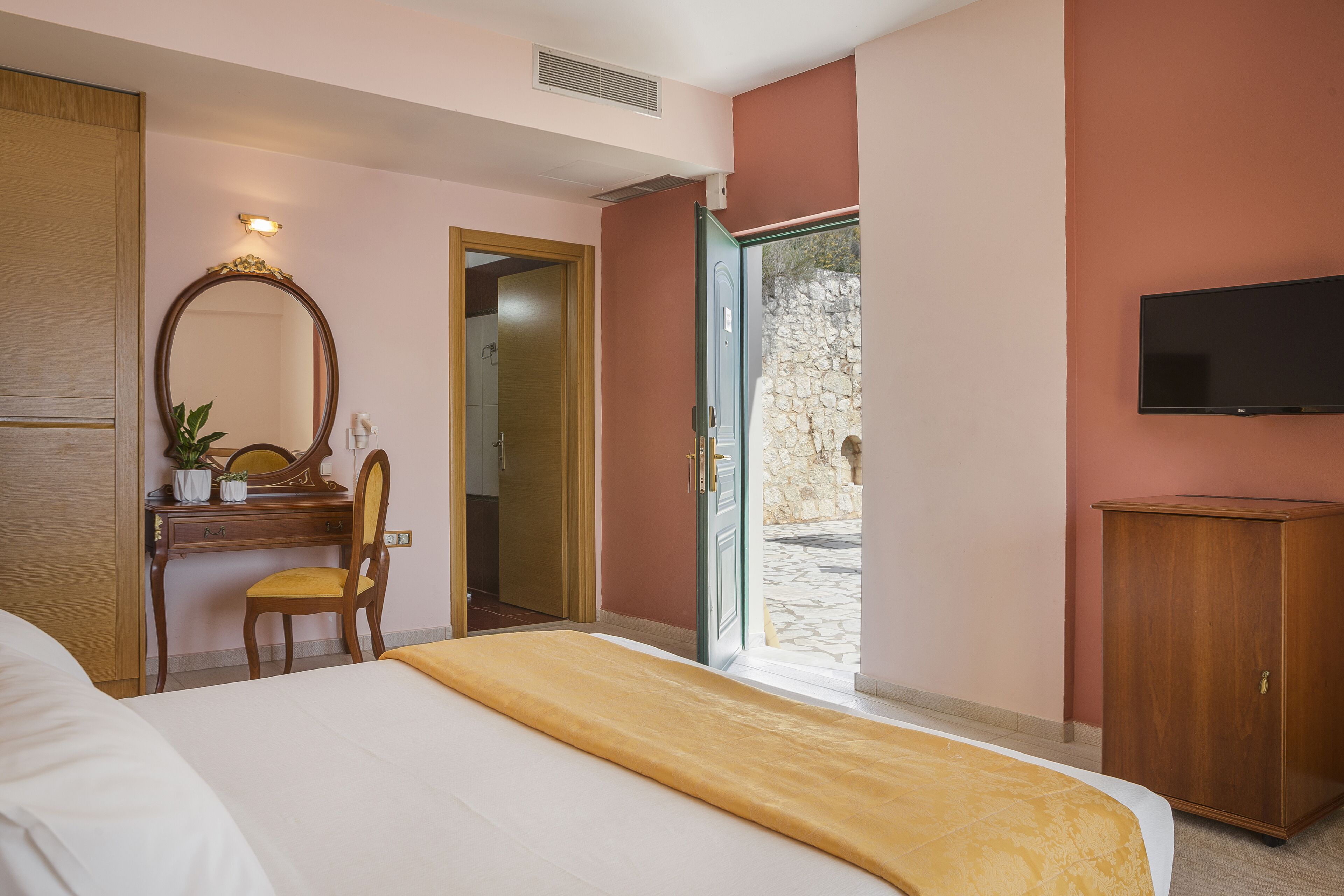 Une chambre d’hôtel comprenant un lit, un bureau avec une chaise, un miroir, une armoire et un téléviseur.