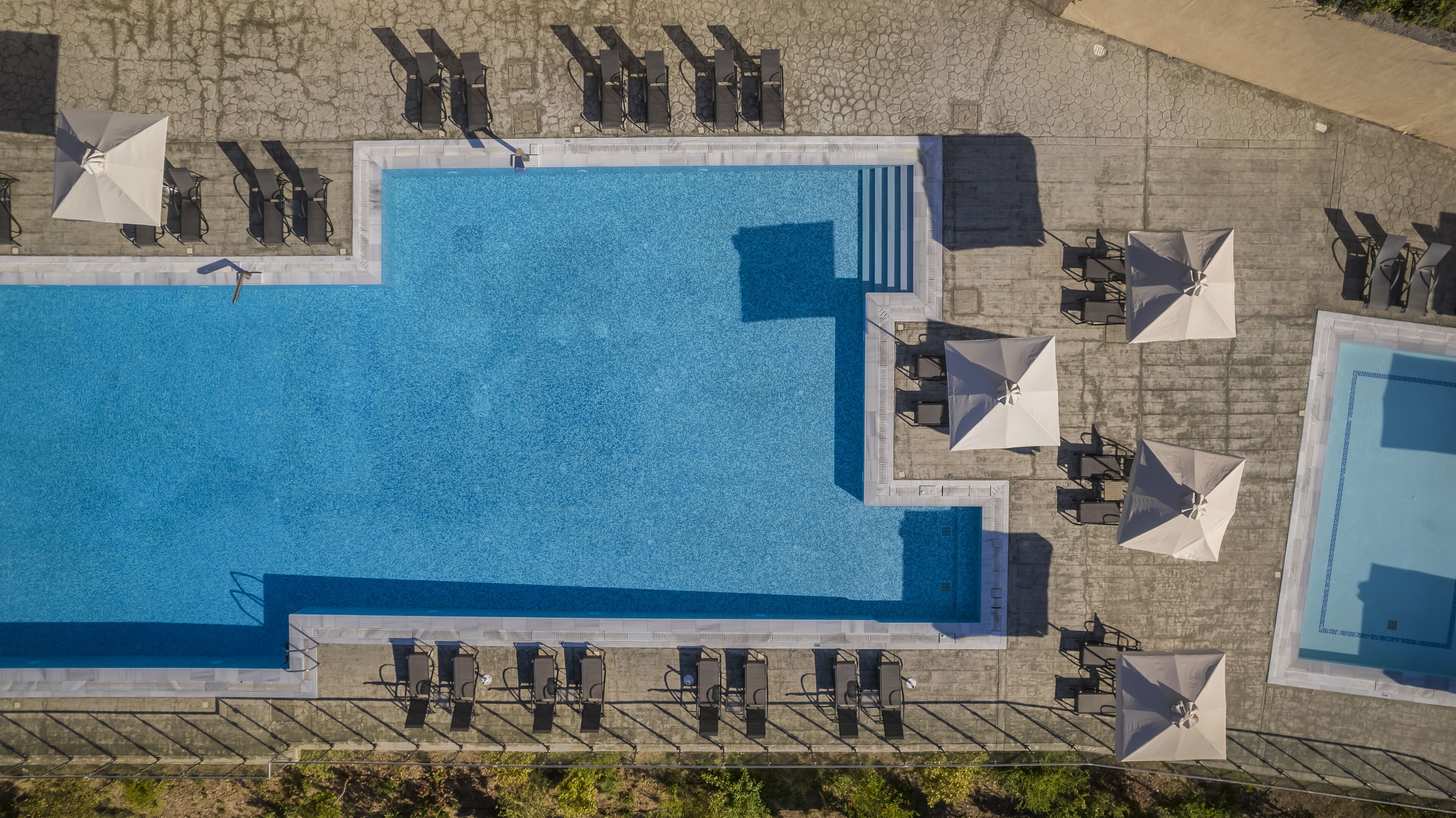 An aerial view of a rectangular swimming pool with multiple lounge chairs and umbrellas around it.