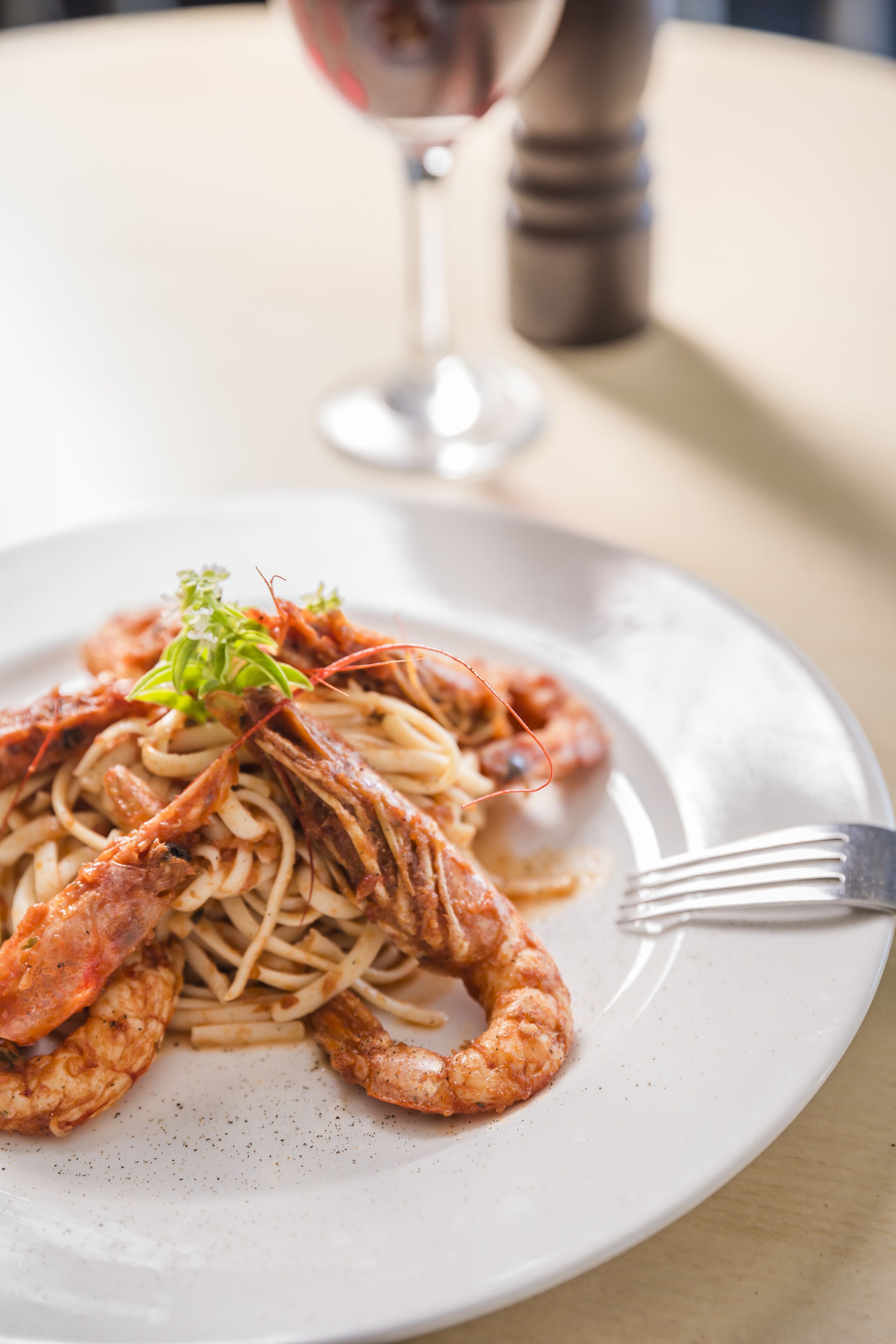 A plate of pasta with shrimp and a small garnish, accompanied by a fork on a table.