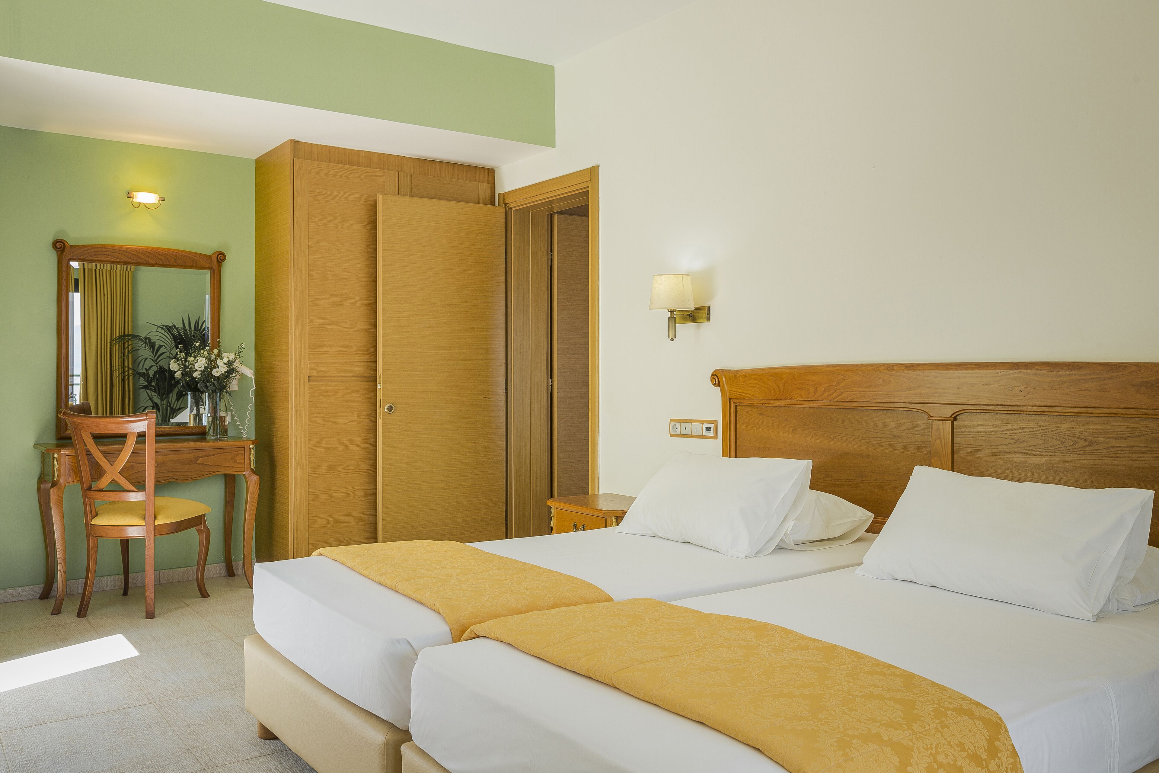 A hotel room with two beds, a desk with a chair, a mirror, and a lamp.