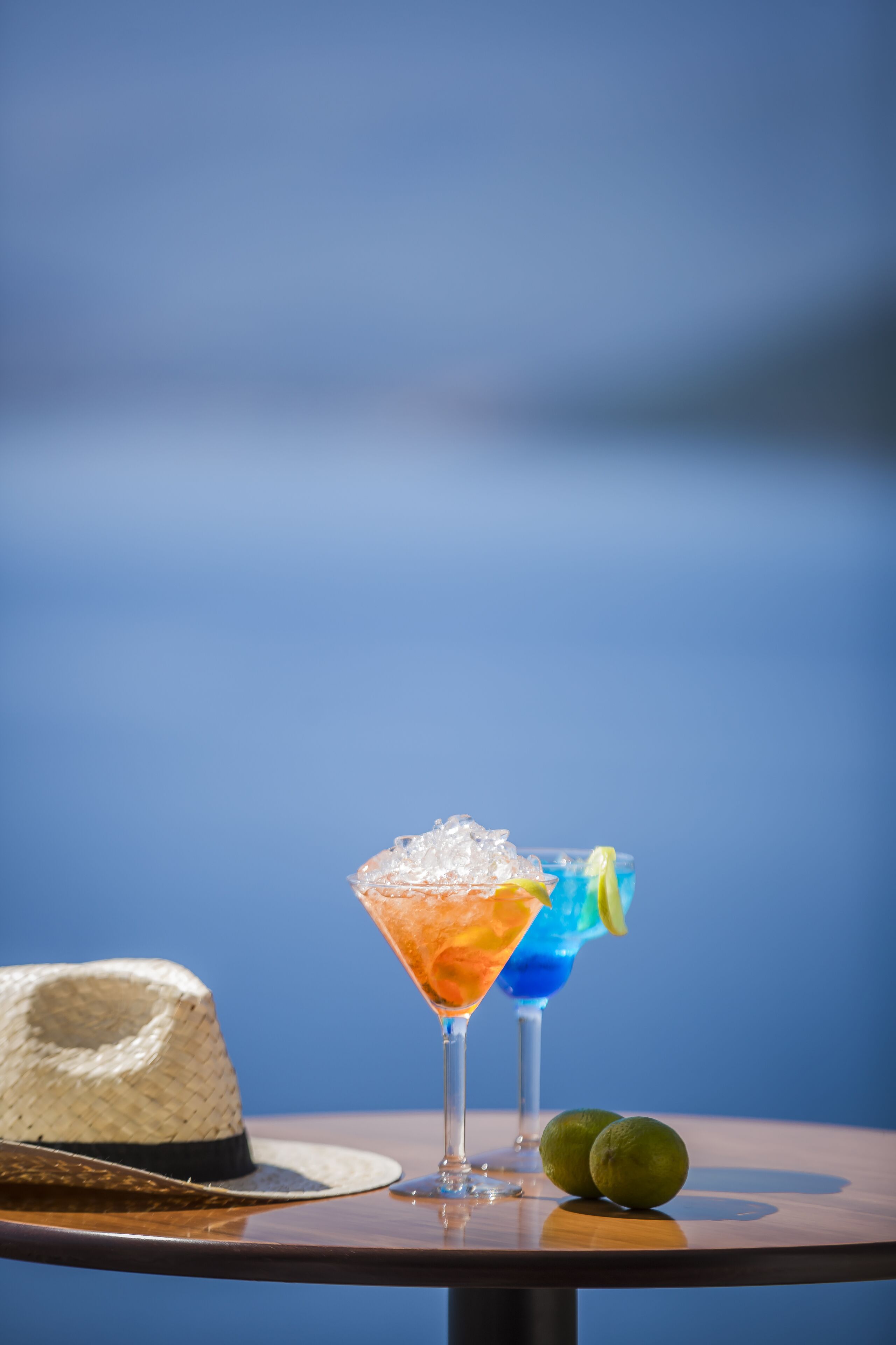 Twee cocktails op een tafel, met een strohoed en limoenen.
