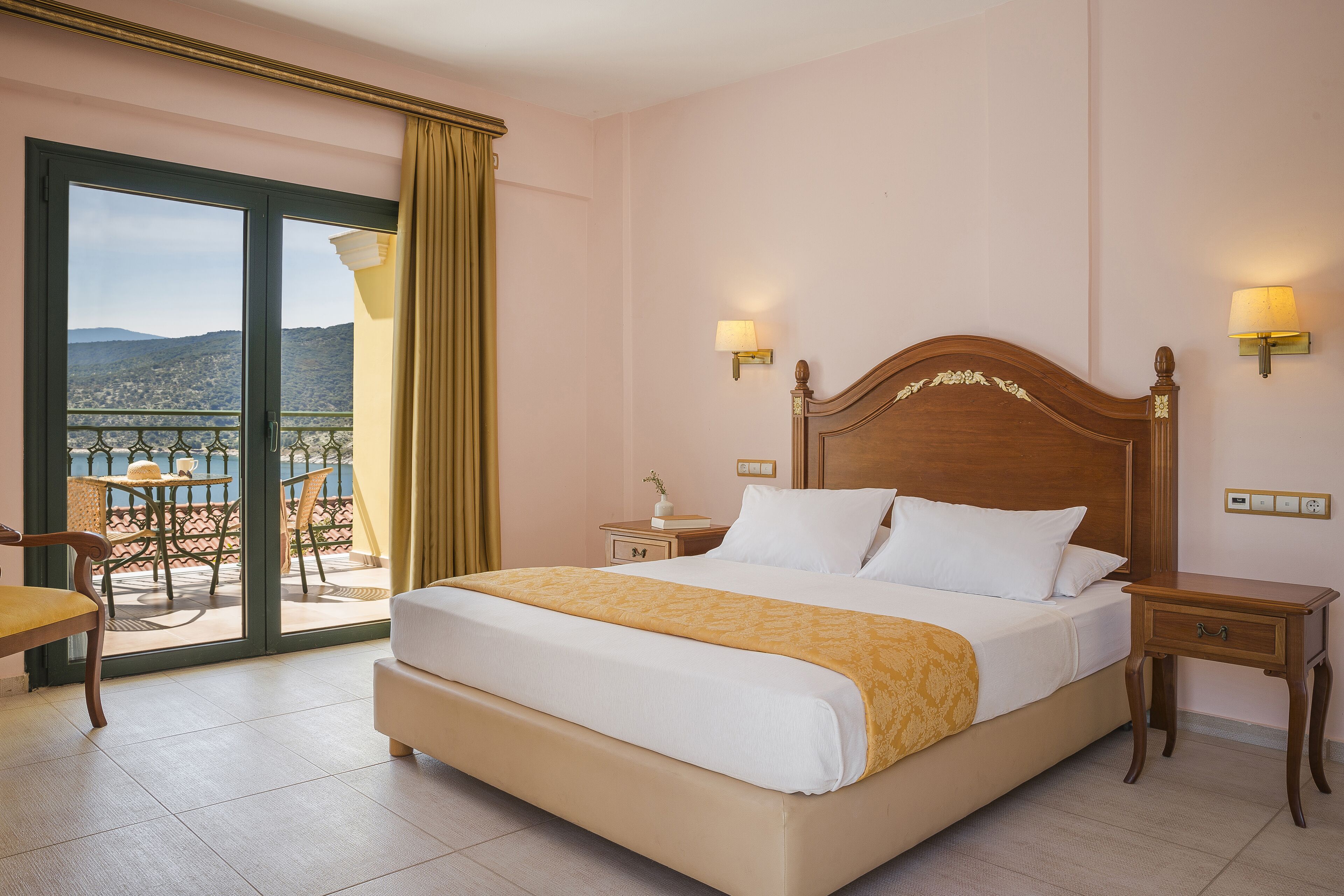 Ein Hotelzimmer mit einem großen Bett, zwei Nachttischen, einem Sessel, einem Balkon mit Tisch und Stühlen und Blick auf die Berge.