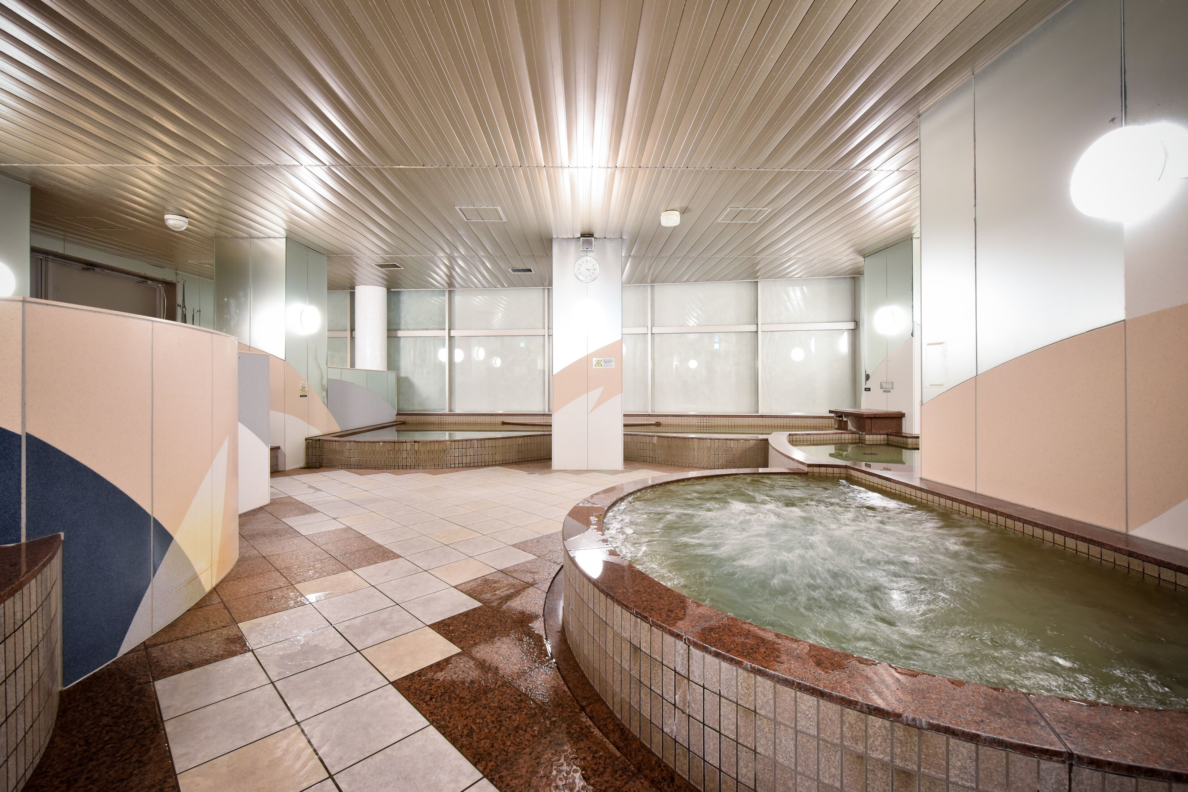 Un espace spa comprenant plusieurs bains à remous, un sol carrelé et un plafond doté de luminaires linéaires.