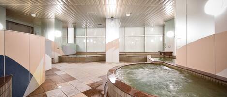 Un espace spa comprenant plusieurs bains à remous, un sol carrelé et un plafond doté de luminaires linéaires.