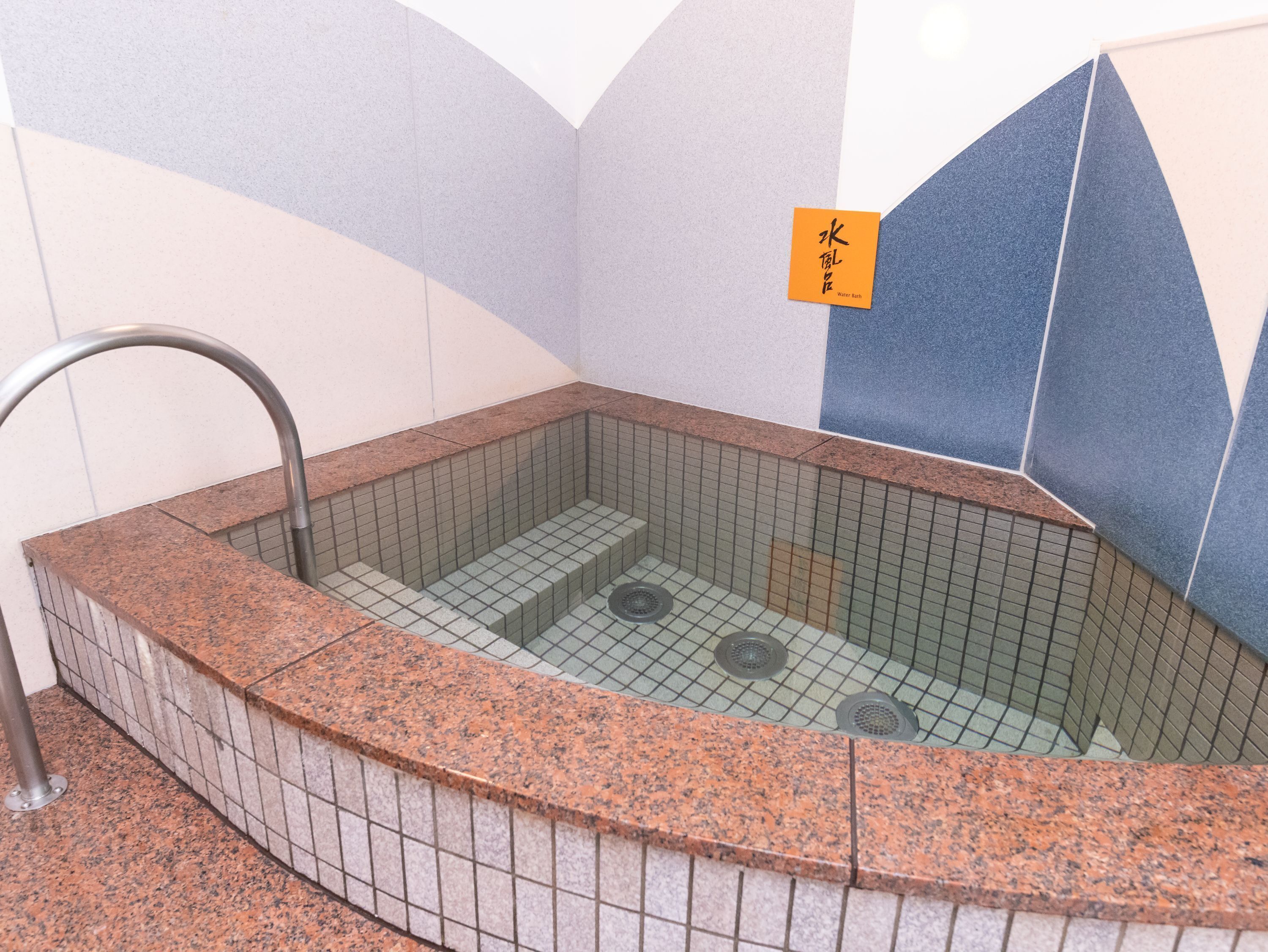 A small, rectangular hot tub with a tiled interior and a metal faucet.