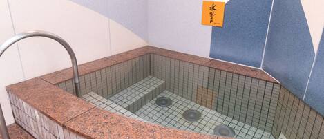 A small, rectangular hot tub with a tiled interior and a metal faucet.