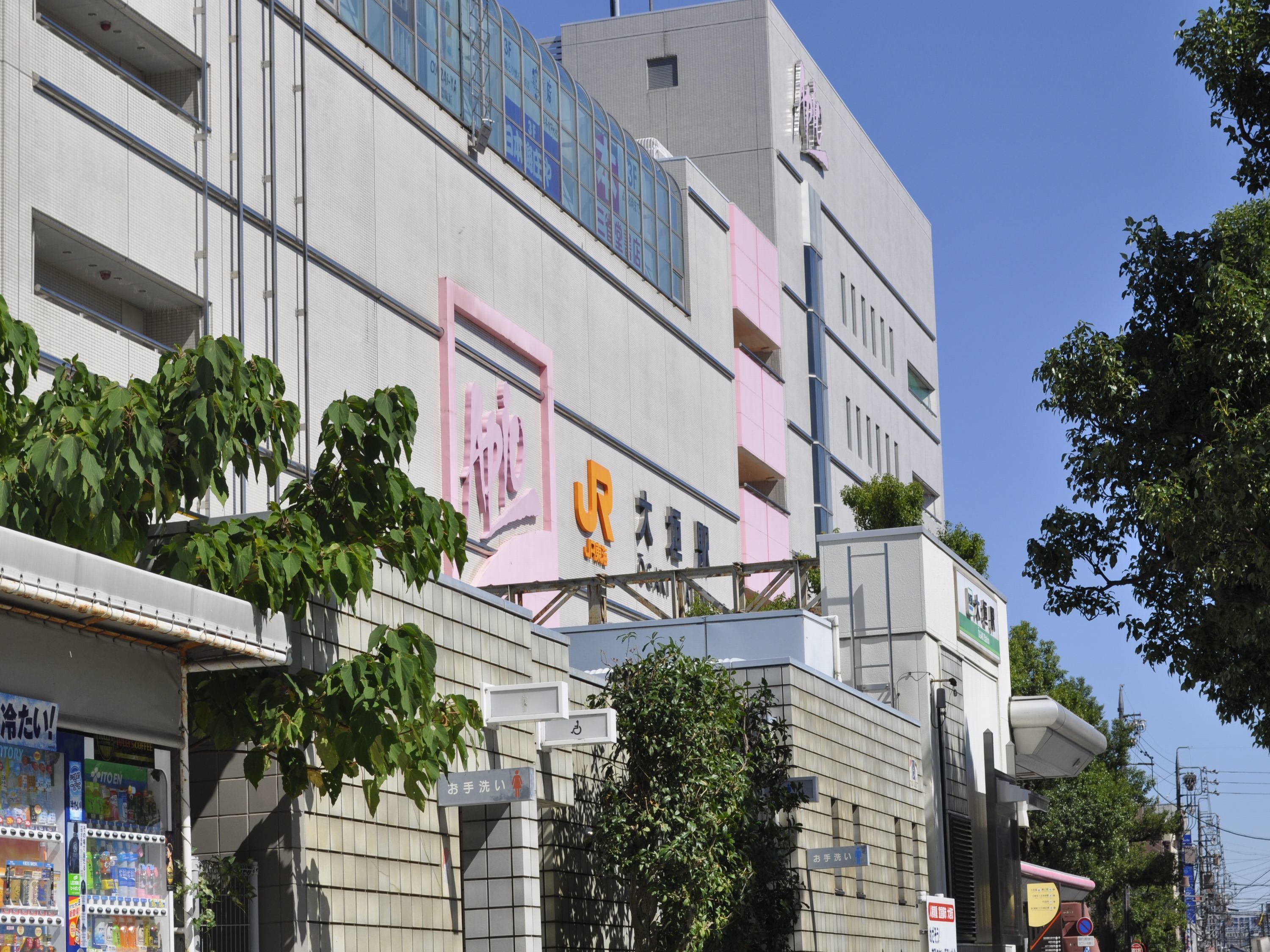 A modern building with a large sign featuring Japanese characters, a visible entrance, and a vending machine on the ground floor.