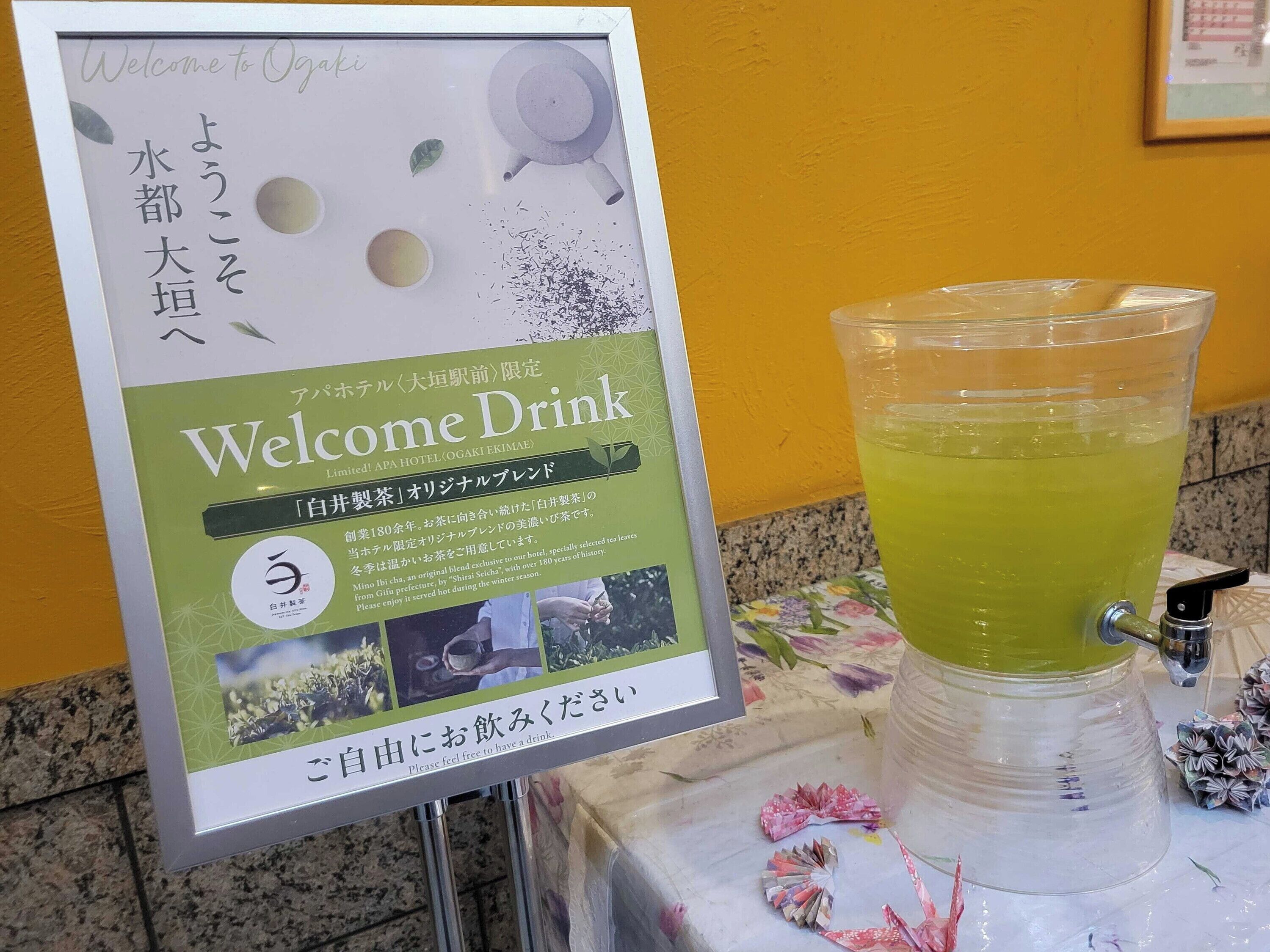 A Welcome Drink sign with Japanese text and a green beverage dispenser.