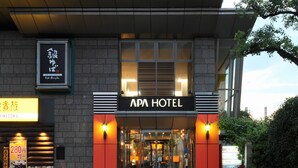 Das äußere Erscheinungsbild des APA HOTEL mit moderner Fassade, großem Glas Eingang und einer markanten Beschilderung.