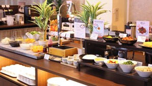 Ein Buffet mit verschiedenen Speisen, darunter Obst, Gemüse und Gerichte in Schalen, mit Schildern, die die verschiedenen Essensbereiche kennzeichnen.