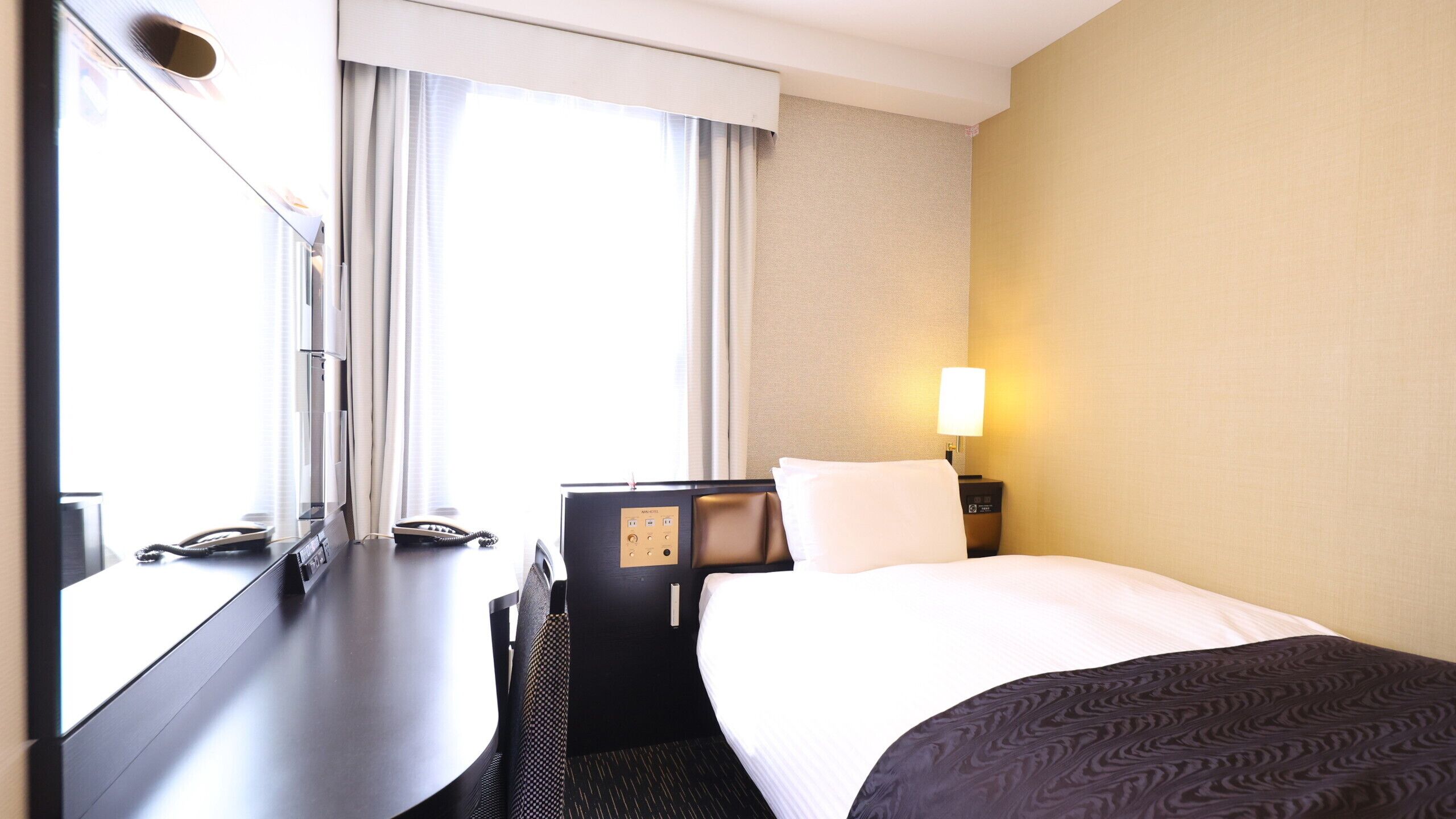 Una habitación de hotel con una cama, un escritorio, un teléfono y una lámpara.