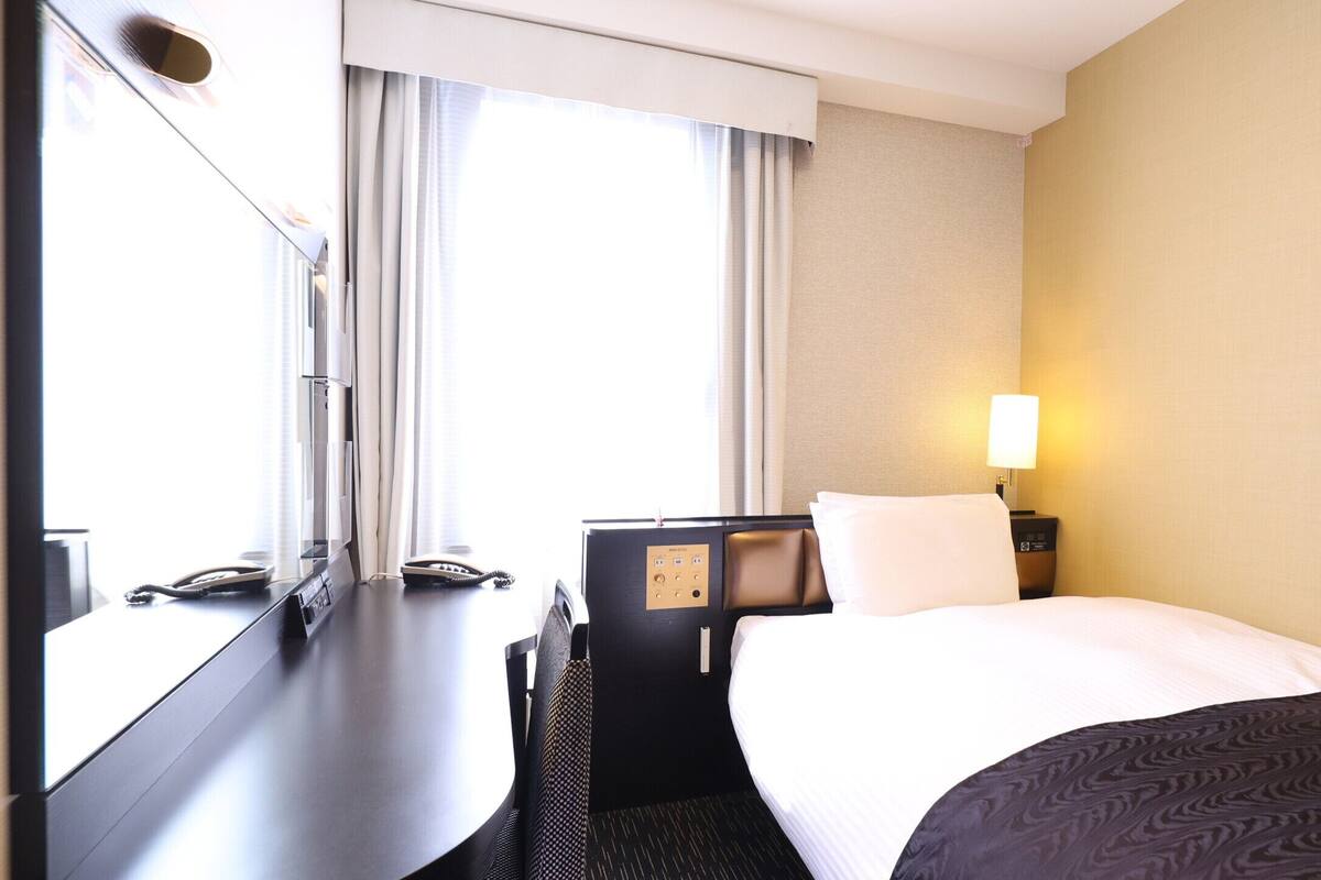 Ett hotellrum med en säng, ett skrivbord, en telefon och en lampa.